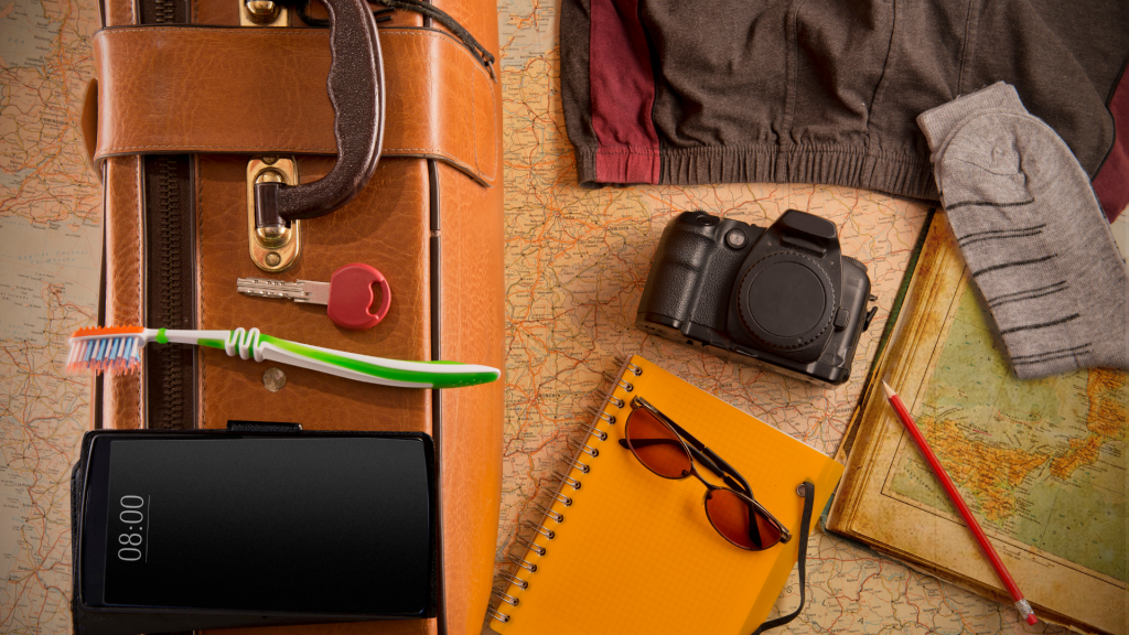 close up of travel essentials: clothes, camera, sunglasses, toothbrush, key, phone, notepad and suitcase.